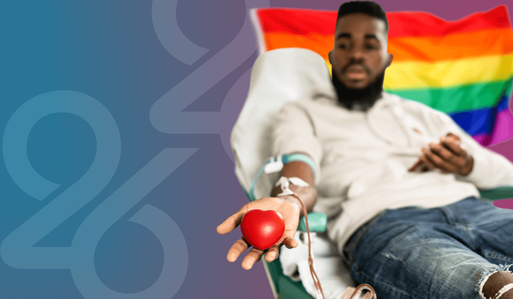 Blurred image of person in grey jacket and jeans laying on bed donating blood with arm extended out with red stress ball in hand