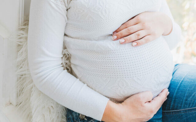 Pregnant woman in white holding belly