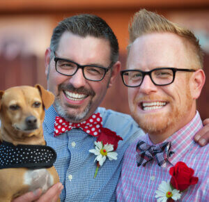 Portrait of smiling couple in colorful clothing wearing black eye glasses while holding dog
