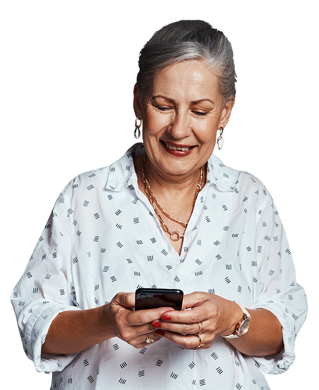 A woman with short gray hair, wearing a white patterned blouse and gold jewelry, is smiling while looking at her smartphone in sunny Orlando.