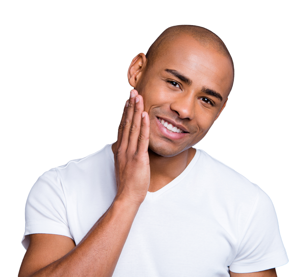 A smiling person with short hair in a white t-shirt, touching their cheek with their right hand. The background is plain and neutral.