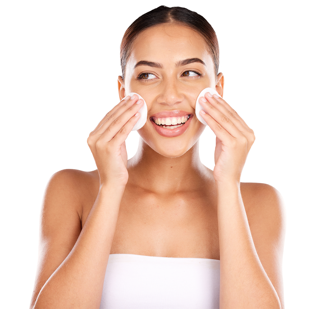 A woman with dark hair is smiling and using two cotton pads to cleanse her face. She is wearing a white strapless top and has a fresh and happy expression. The background is plain white.