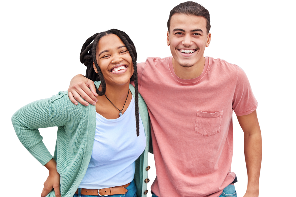 Two people, one wearing a green cardigan over a light blue shirt and the other wearing a pink shirt, smile broadly at the camera. They stand close together, with one person's arm around the shoulder of the other, suggesting a warm and friendly relationship.