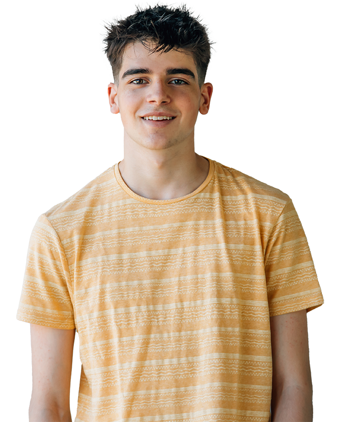 A young person with short, slightly tousled dark hair is smiling while standing and looking forward. They are wearing a yellow, short-sleeved shirt with a subtle, horizontal striped pattern. The background is plain and light.